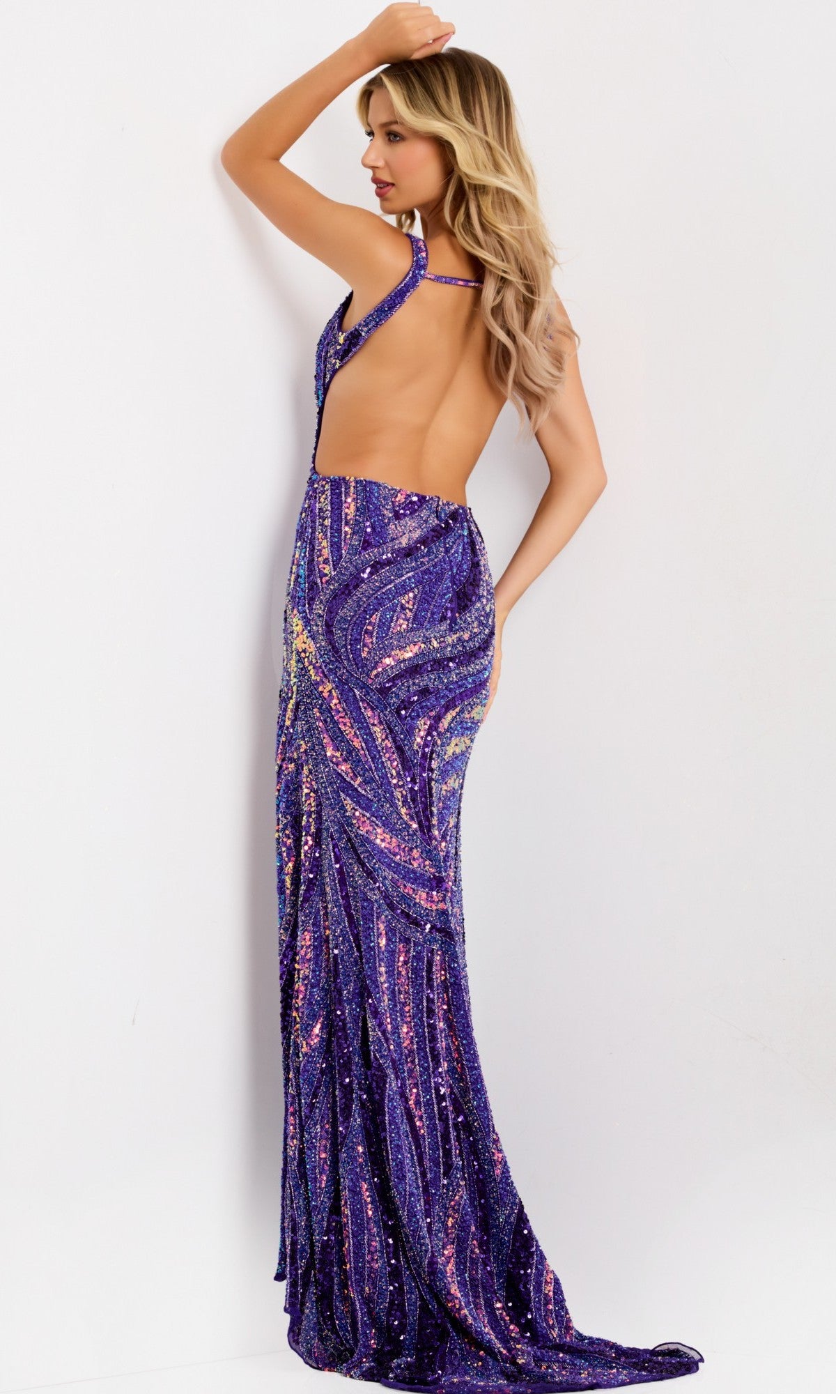 A woman with long blonde hair wears the Jovani 47793 Long Prom Dress—a floor-length purple gown with swirling sequin patterns and an open back—posing with one arm raised against a plain white background.